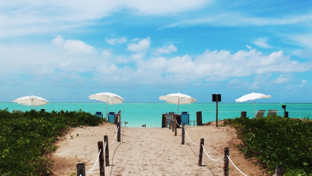 O caminho de areia para praia do Morro, com um mar verde claro e um céu azul.