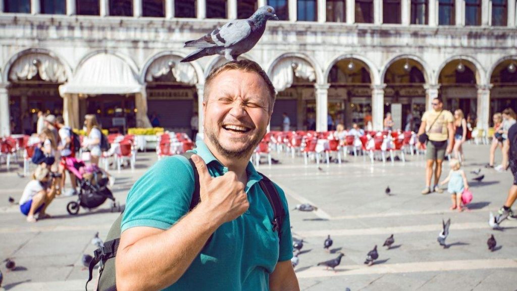 Homem sorridente e feliz, com pomba na cabeça na Piazza San Marco em Veneza, Itália. 