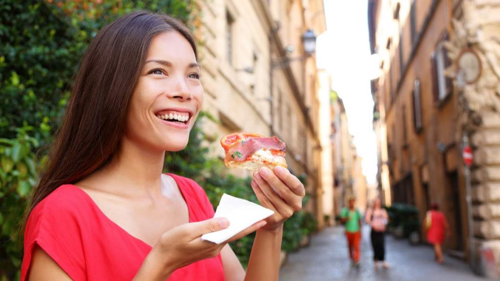 Mulher comendo uma fatia da pizza em Roma, Itália