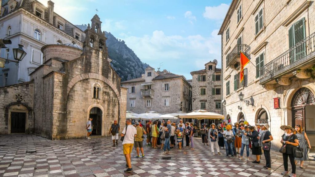 Os turistas se reúnem na praça de São Lucas, em frente à igreja antiga, com suas três torres sineiras em Kotor, Montenegro.